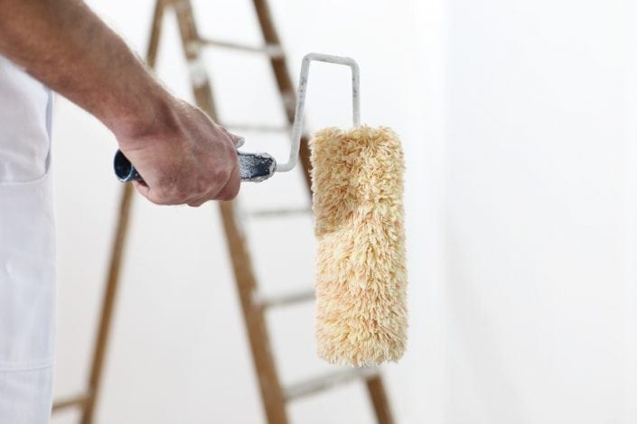 painter man at work with a paint roller and ladder, hand clsose up